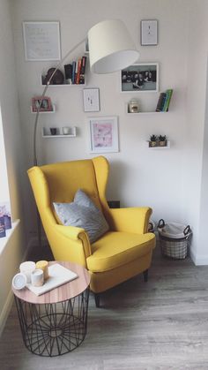 a yellow chair sitting in a living room next to a table with a cup on it