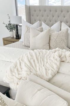 a white bed with pillows and blankets on it in a bedroom next to a window