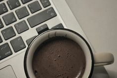 a cup of hot chocolate sitting on top of a laptop computer next to a keyboard