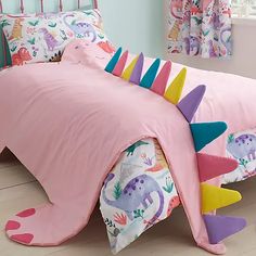 a child's bed with pink sheets and colorful dinosaurs on the pillowcases