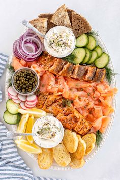 a platter with smoked salmon, cucumbers, pickles and crackers