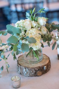 a vase filled with white flowers and greenery on top of a wooden table next to candles