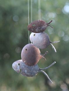 three metal birds hanging from strings in front of trees