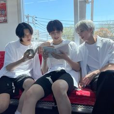 three young men sitting on a bench looking at an electronic device in front of them