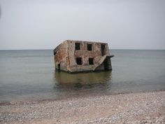 an old concrete structure sitting in the middle of the ocean on top of a sandy beach