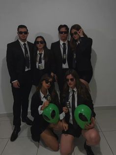 a group of people in suits and sunglasses posing for a photo with green balloons on the floor