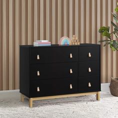 a black dresser with gold handles in front of a striped wallpapered background and a potted plant