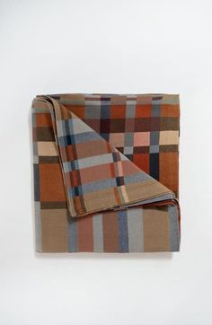 a plaid blanket is folded on top of a white wall and it's brown, blue, orange, and tan color scheme