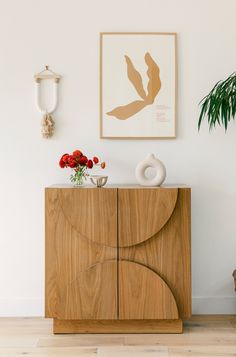 a wooden cabinet sitting next to a plant on top of a hard wood floor