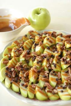 a white plate topped with sliced apples covered in caramel and pecans next to an apple