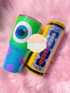 two colorful cups sitting next to each other on a pink fur covered surface with an eyeball stick in the middle