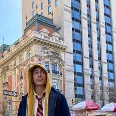 a young man in a hoodie is standing on the street with buildings behind him