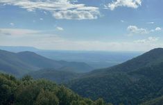 the mountains are covered in green trees and blue sky with fluffy white clouds above them