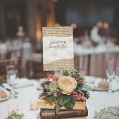 a table topped with books covered in flowers and greenery next to a white table cloth