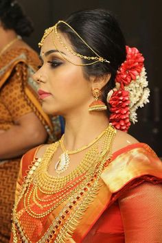 a woman in an orange and gold sari with jewelry on her head, looking off to the side