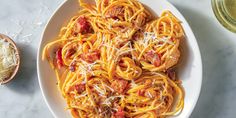 pasta with tomato sauce and parmesan cheese on a plate next to a glass of wine