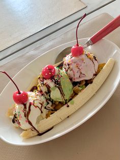 a banana split with ice cream and cherries on top in a white bowl sitting on a table