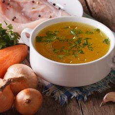 a white bowl filled with soup next to carrots and other vegetables on a wooden table