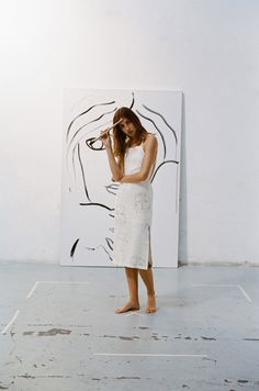 a woman standing in front of a painting holding a cell phone to her ear and looking at it