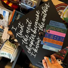 a person holding up a graduation cap with writing on it and some books in the background