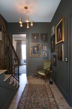 the hallway is decorated in gray and features pictures on the wall, rugs, and chandelier