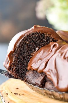 a piece of chocolate cake with frosting on a wooden board next to a knife