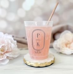 a pink drink sitting on top of a white table next to flowers and a wooden stick