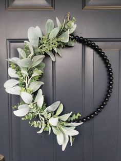 a black beaded wreath hanging on the front door with greenery and leaves around it