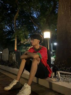 a man sitting on the ground next to a tree at night with his legs crossed