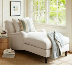 a white couch sitting in front of a window next to a table with books on it