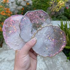 a hand holding three pieces of glass in front of some plants and flowers on the ground