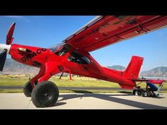 a red airplane parked on top of an airport tarmac next to a man working on the wing