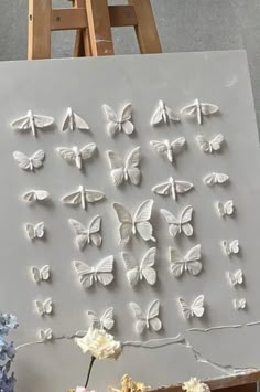 some white butterflies are on a canvas next to flowers