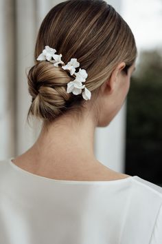 a woman with her hair in a low bun, wearing a white dress and flowers in her hair