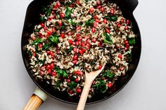 a skillet filled with rice, spinach and pomegranates next to a wooden spoon