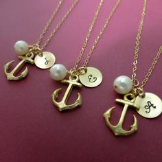 three personalized necklaces with an anchor, pearl and initial charm on a pink background