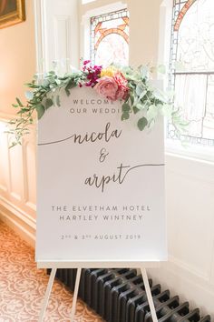 a welcome sign with flowers and greenery on it in front of a radiator