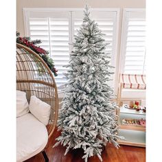 a white christmas tree sitting in front of a window next to a wicker chair