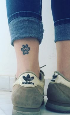 a woman's foot with a paw tattoo on her left ankle and an adidas sneaker