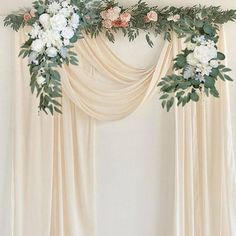 an arrangement of flowers and greenery is hanging on the wall next to a drape