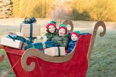 two children in a sleigh with presents on the back and one child wearing knitted hats