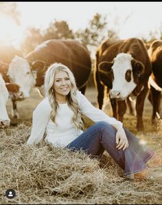 a woman sitting on the ground in front of cows