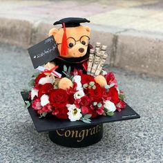 a graduation teddy bear sitting on top of a hat with flowers in it's lap