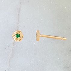 a pair of gold ear studs with a green stone in the middle, on a white background