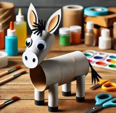 a donkey made out of toilet paper sitting on top of a wooden table next to paint supplies