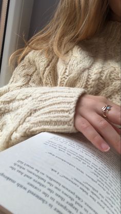 a woman is reading a book and wearing a ring