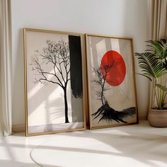 two framed art pieces sitting on top of a white table next to a potted plant