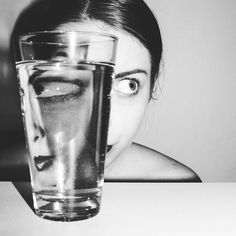 a woman is looking at a glass of water with her face in the glass,