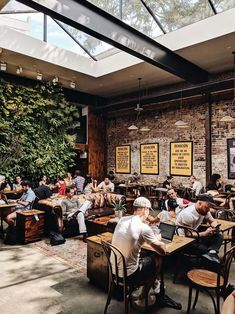 many people are sitting at tables in a restaurant with brick walls and green plants on the wall