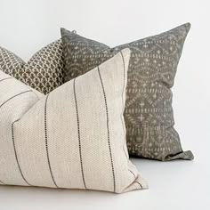 two decorative pillows sitting next to each other on a white surface, one is black and the other is beige